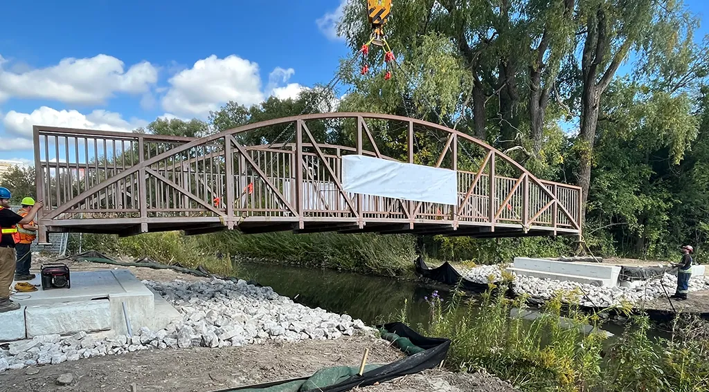 A walking bridge in a park being lowered into place over a stream.