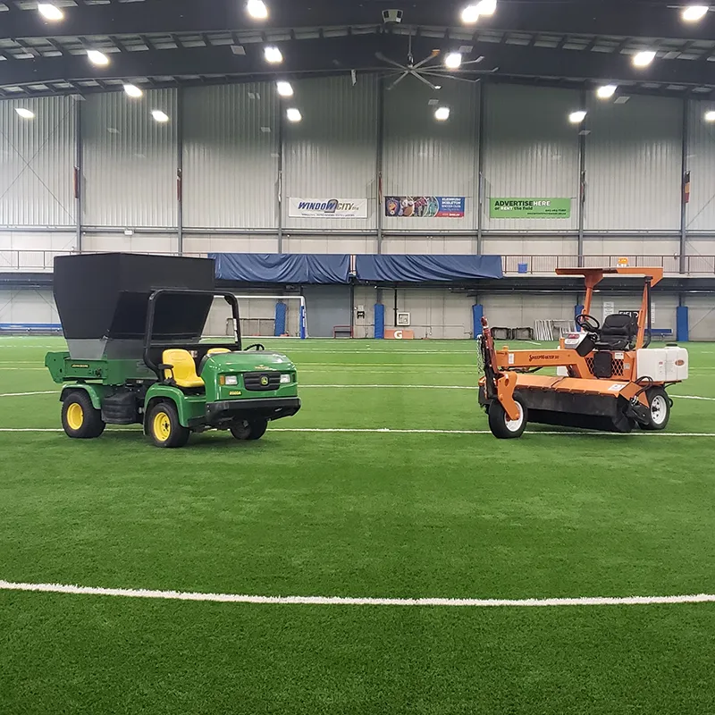Turf maintenance machines sit parked on an indoor soccer field.