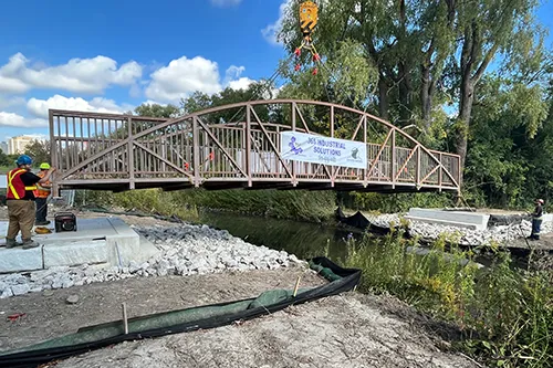 Workers install a bridge over a stream in a park being build by 39 Seven.